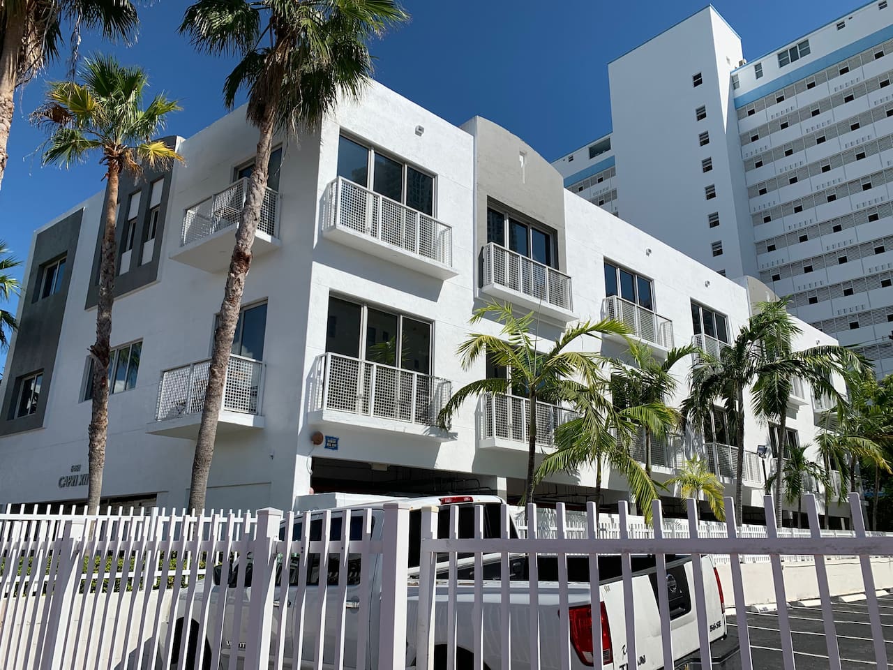 Small townhouse building in classic Miami white with grey accents, framed by palms