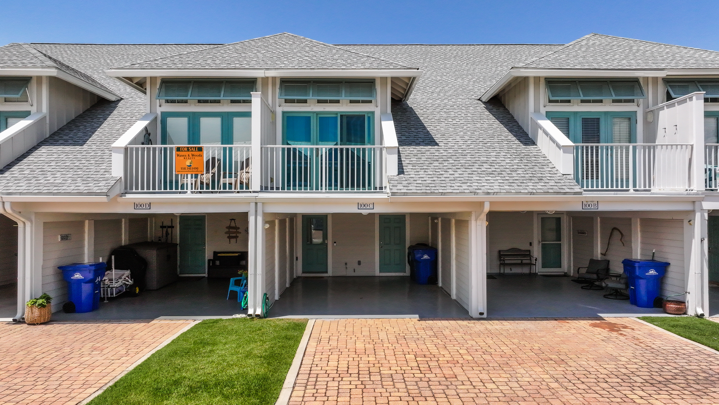 Bright coastal townhome with a private driveway, carport, and a welcoming entrance, perfect for a relaxing beach getaway.