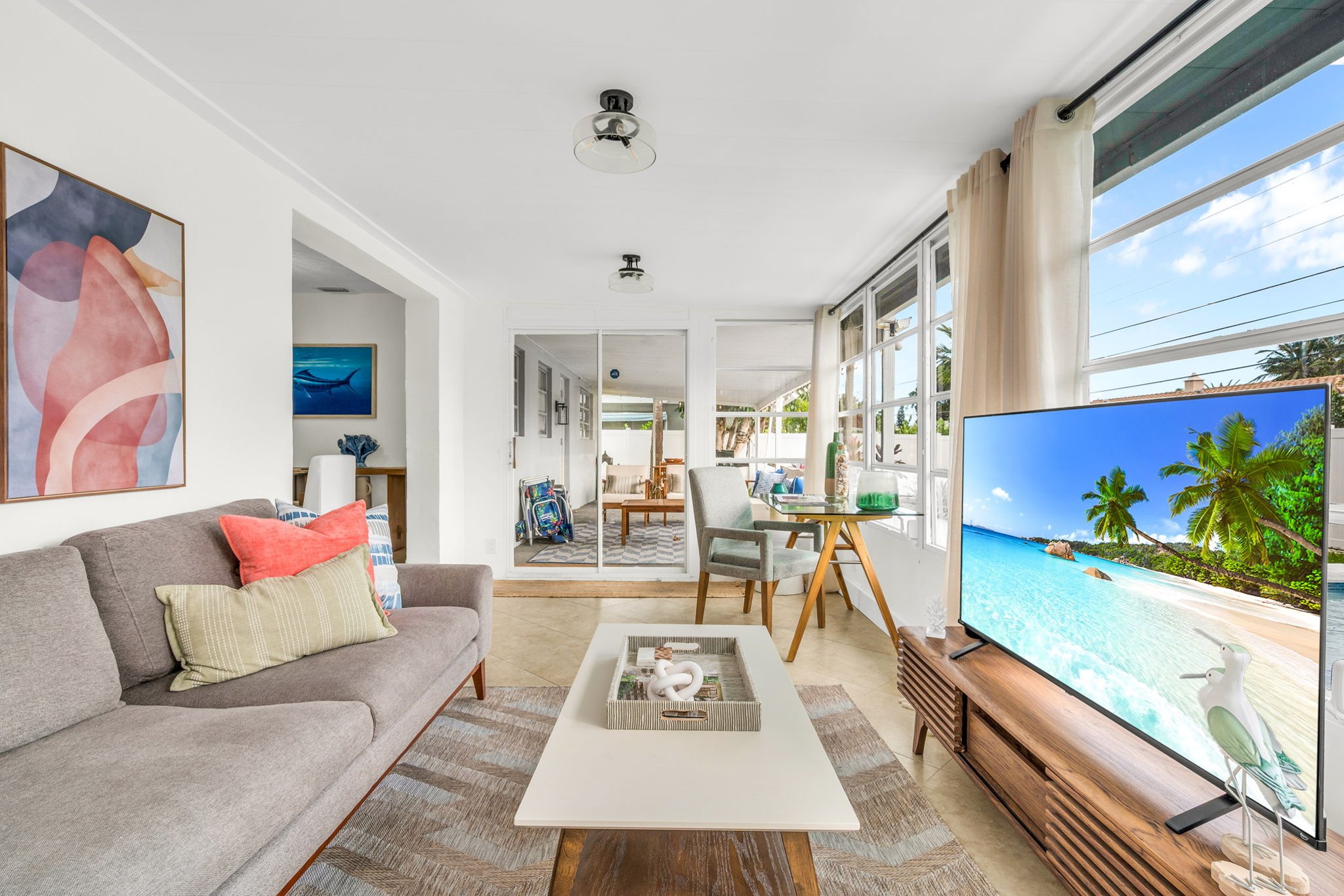 A beautifully designed Florida sunroom with wrap-around windows, modern furnishings, a Smart Fire streaming TV, and tranquil pool views—ideal for lounging, morning coffee, or working in style.