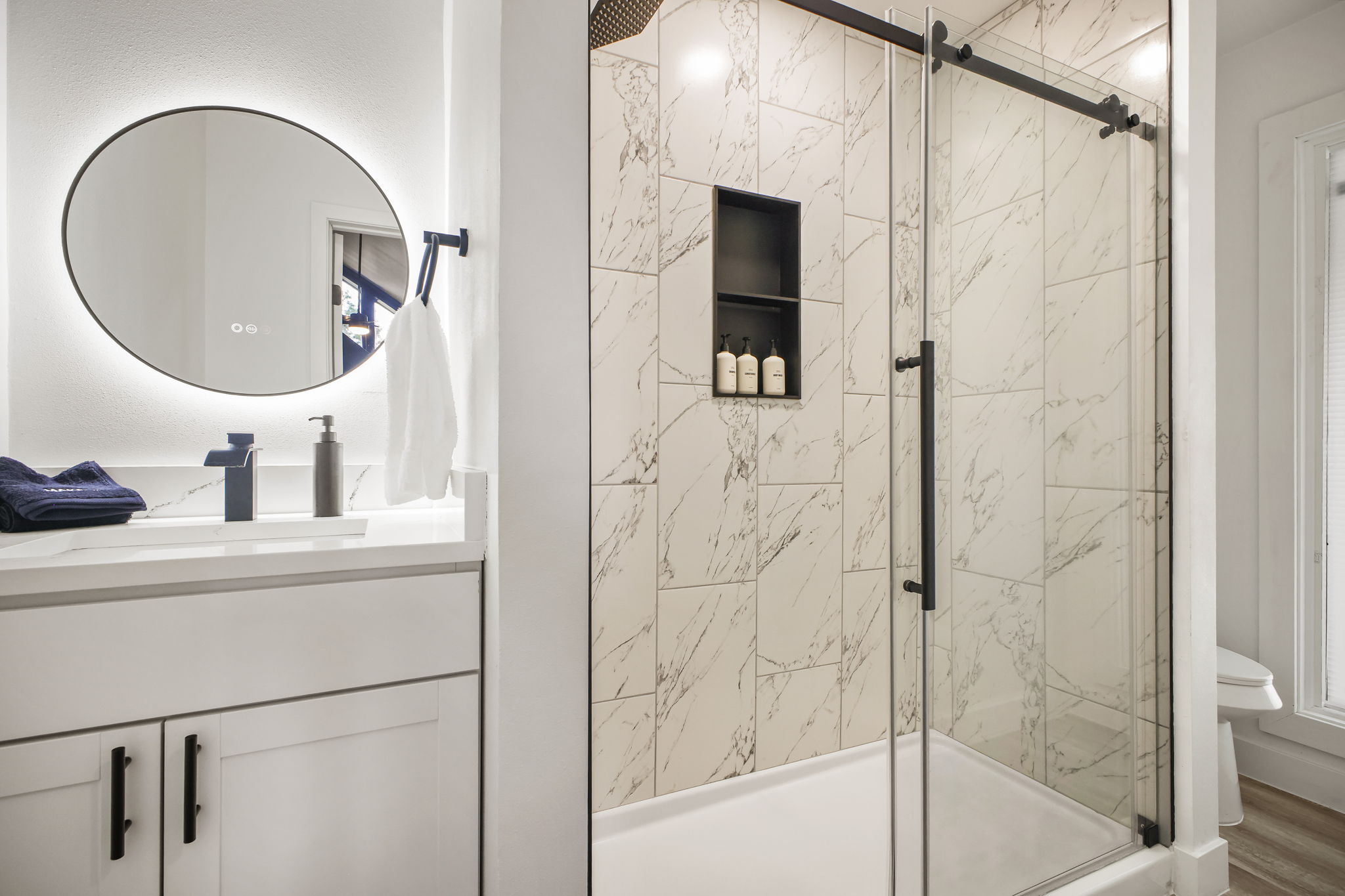 Our main floor full bathroom offers convenience & style with a modern vanity, bright backlit mirror, & sleek glass walk-in shower. Easily accessible, provides a comfortable space for guests.