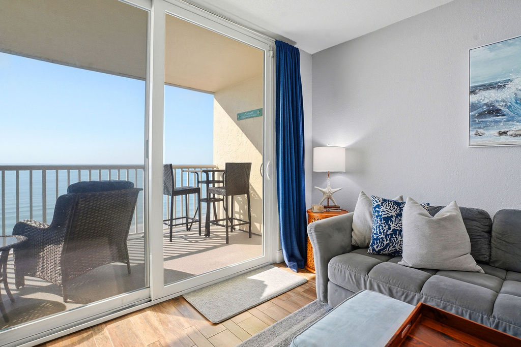 Oceanfront living space with comfortable seating, floor-to-ceiling sliding glass doors, and direct access to a private beachfront balcony with stunning panoramic water views.