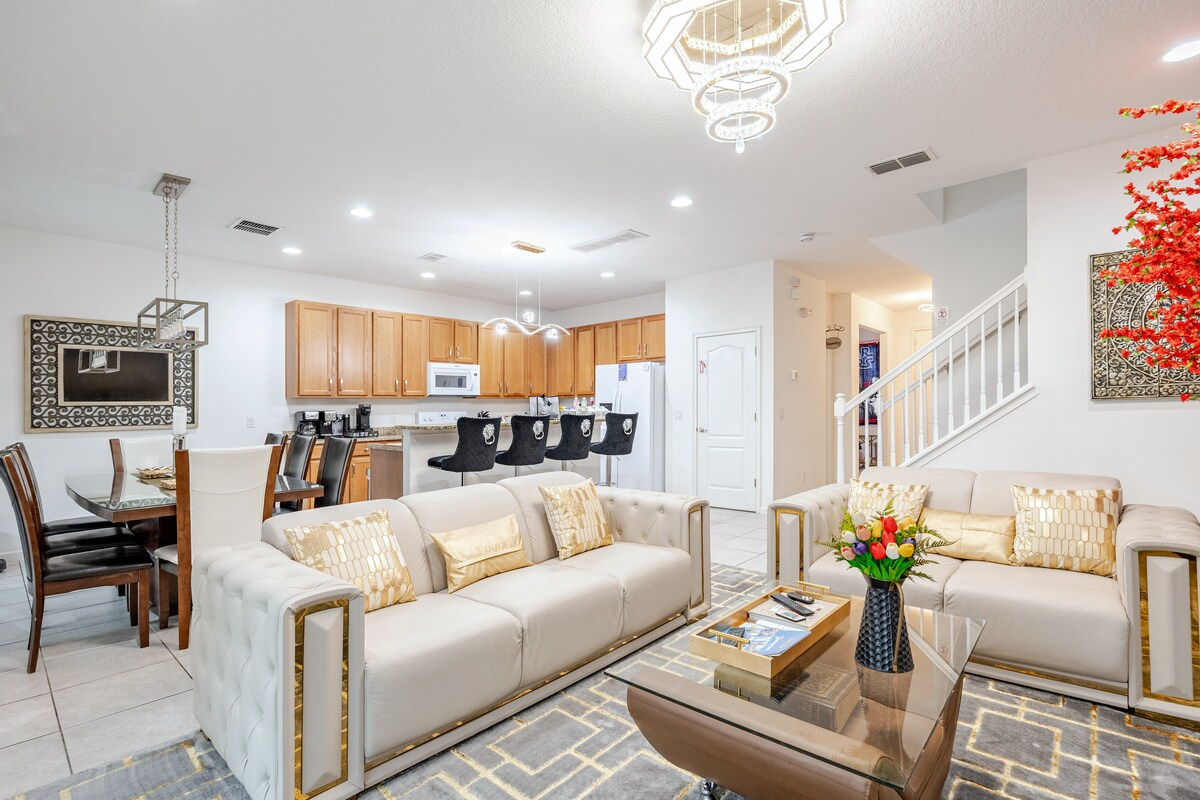 Main downstairs living room with a 98-inch TV and piano, open to the kitchen and dining area.
