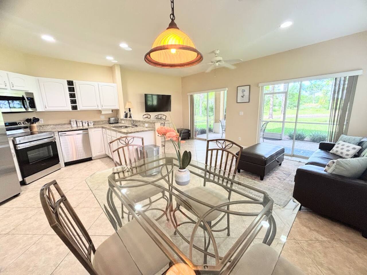 Bright open-concept living and dining area with a fully equipped kitchen, comfortable seating, and sliding glass doors overlooking the greenery.