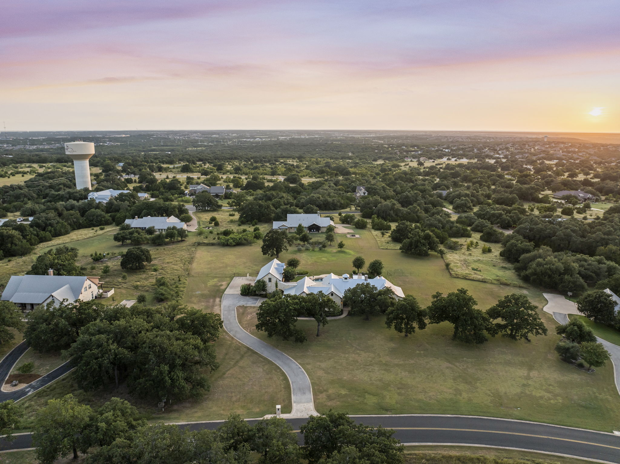 A luxury home surrounded by serene oak trees and rolling green landscapes, bathed in the warm glow of a sunset.
