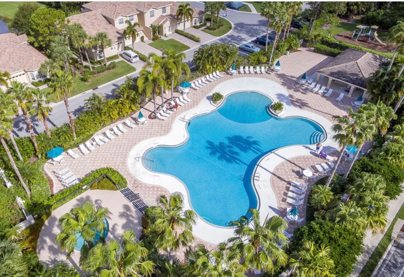 Aerial view of the community pool area featuring a spacious sundeck, lounge chairs, and lush tropical surroundings.