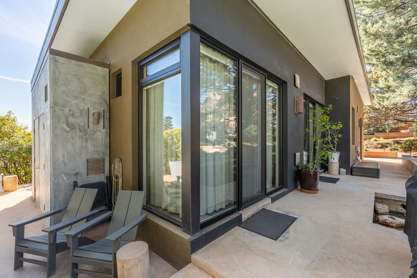 Modern mid-century exterior with floor-to-ceiling glass, private patio seating, and serene surroundings.