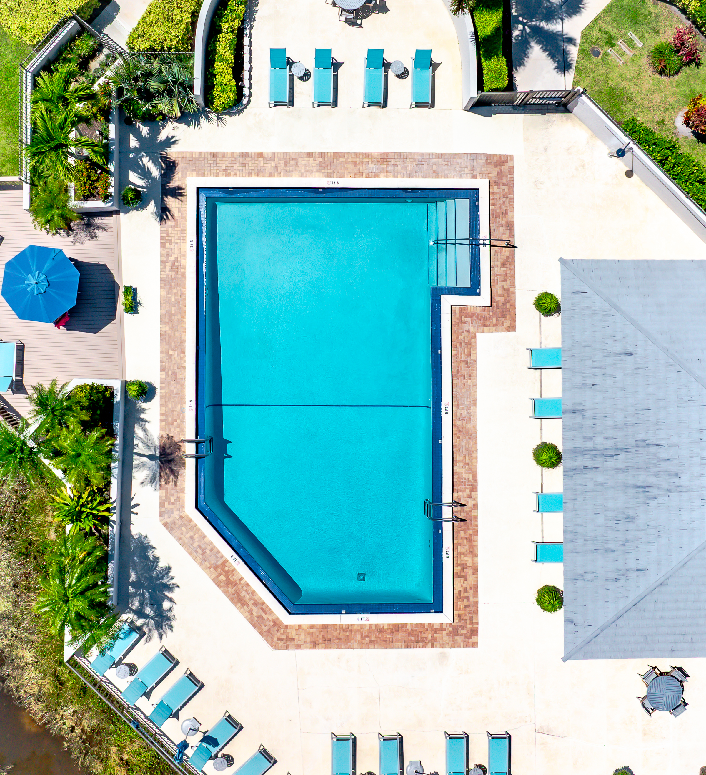Resort-style heated community pool surrounded by lush tropical landscaping, sun loungers, and peaceful lake views — perfect for relaxing after a day at the beach or golf course.
