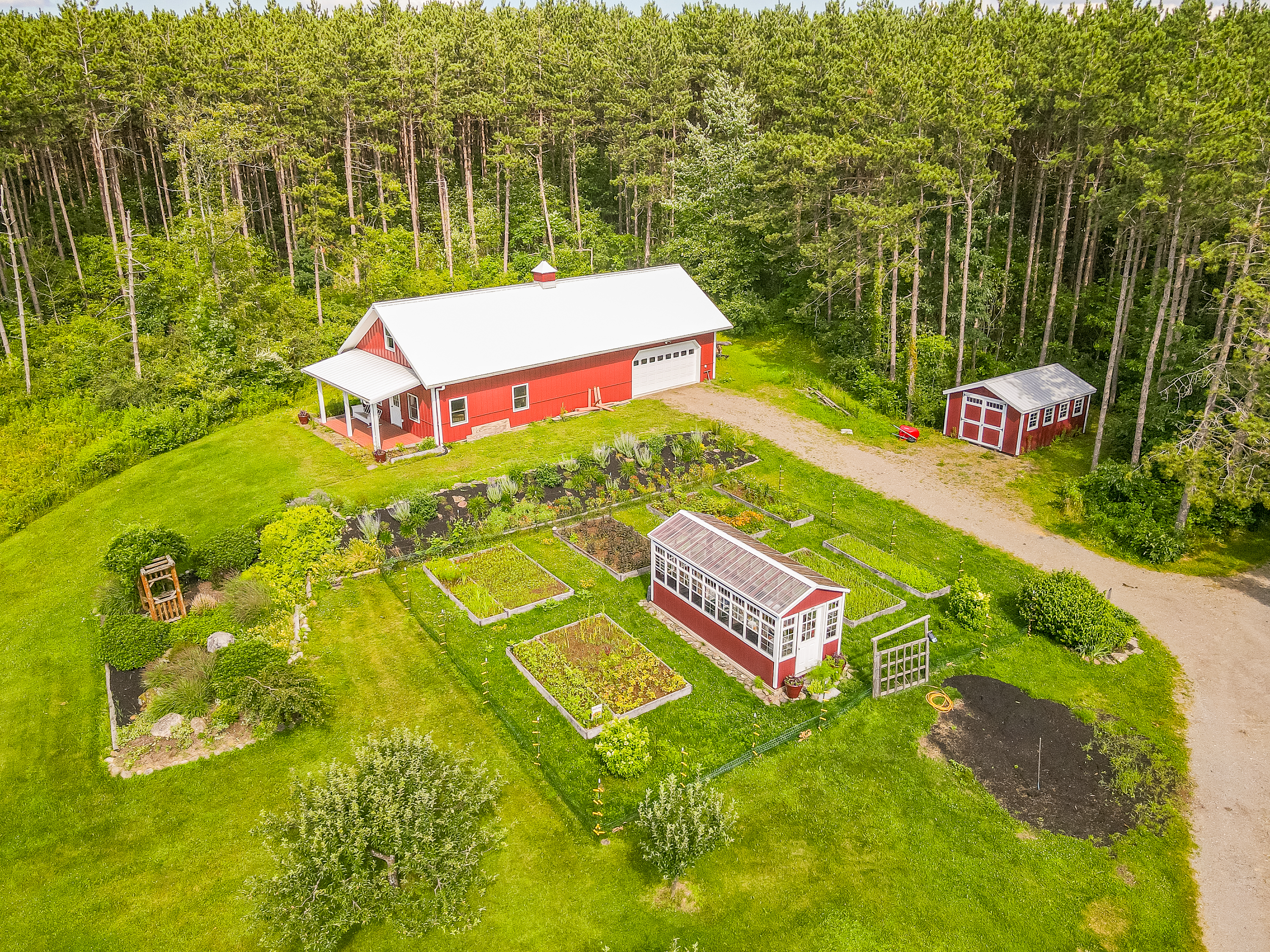 Charming country living with a classic red barn, greenhouse, and lush garden beds surrounded by nature’s beauty.