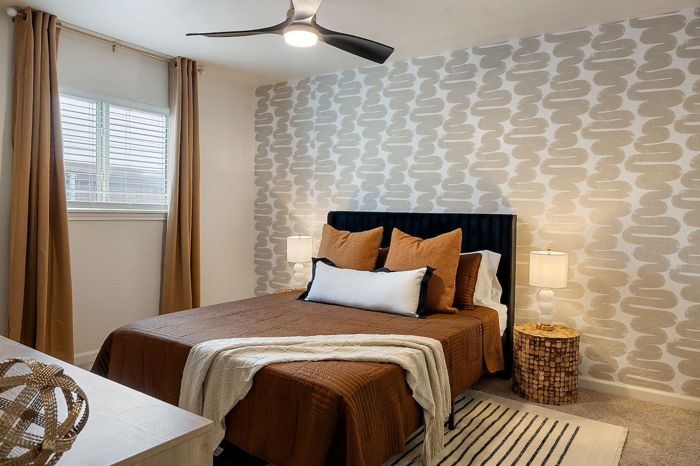 Enjoy a restful night's sleep in this beautifully decorated bedroom with stylish wallpaper and cozy bedding. The ceiling fan provides added comfort.