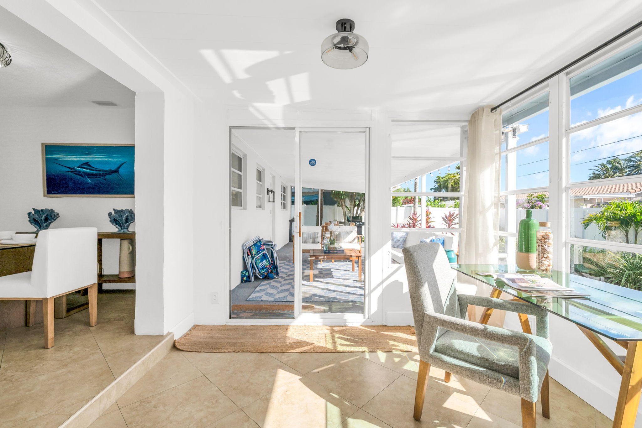 A beautifully designed Florida sunroom with wrap-around windows, modern furnishings, a Smart Fire streaming TV, and tranquil pool views—ideal for lounging, morning coffee, or working in style.