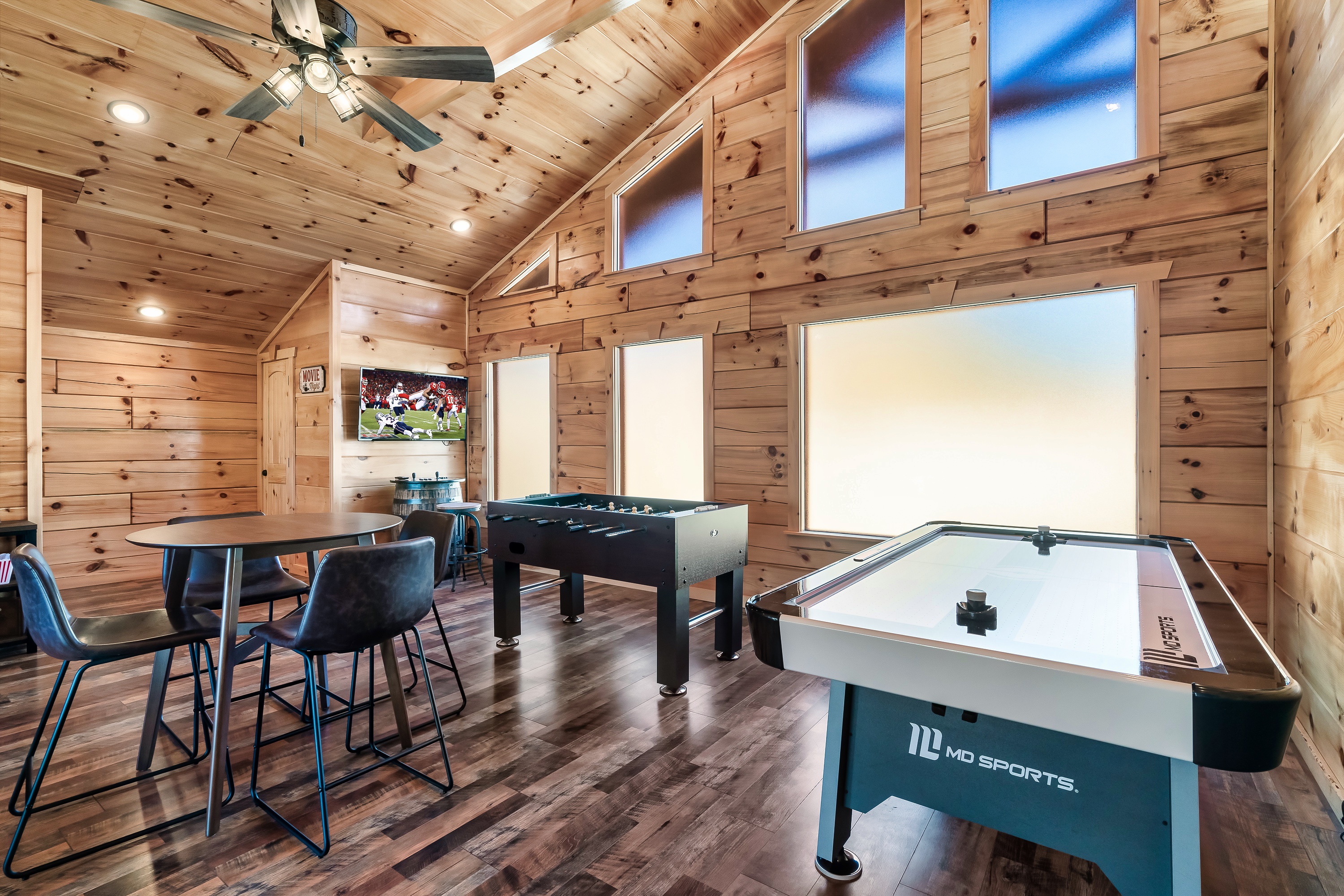 Spacious wood-paneled game room with air hockey, foosball, barrel arcade + smart TV, and high-top cafe seating