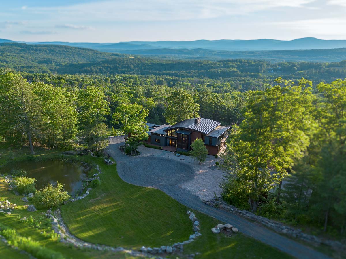 Front of Sunset Falls Estate from above &mdash; the curved roofline and the Berkshires valley beyond at sunset