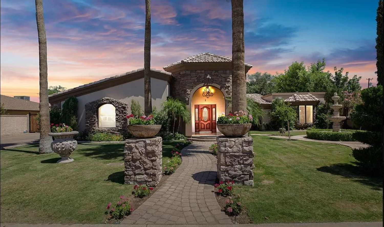 Step into your private oasis, a stone-accented haven surrounded by lush gardens, glowing sunsets, and a grand entrance that warmly welcomes you home.