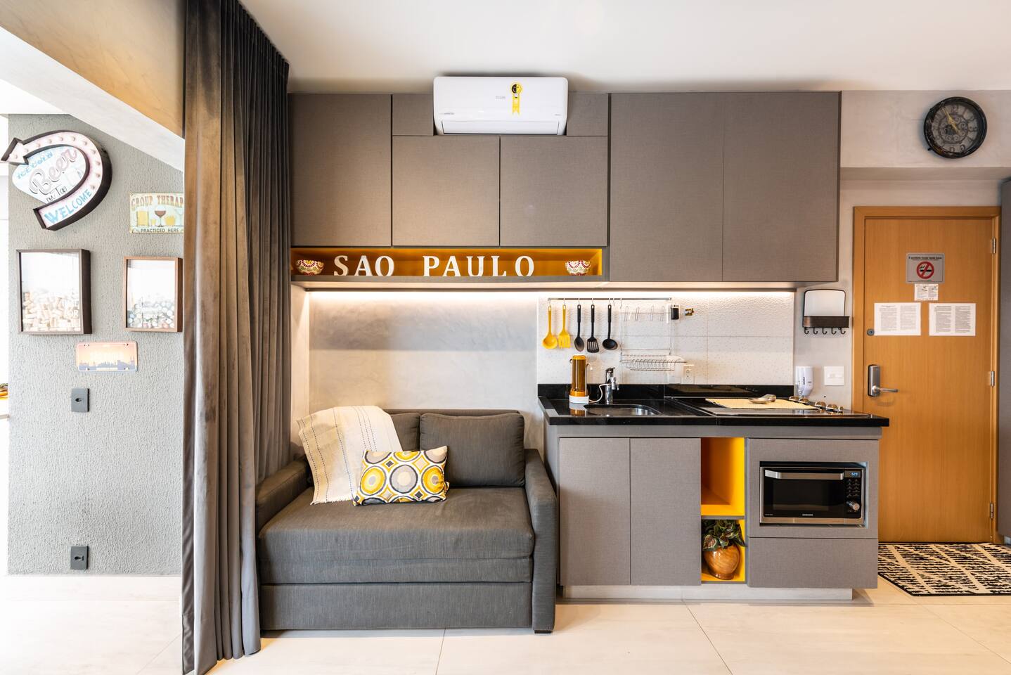Sala de estar aconchegante com sofá moderno, ar-condicionado e cozinha integrada, perfeita para relaxar após explorar Pinheiros.