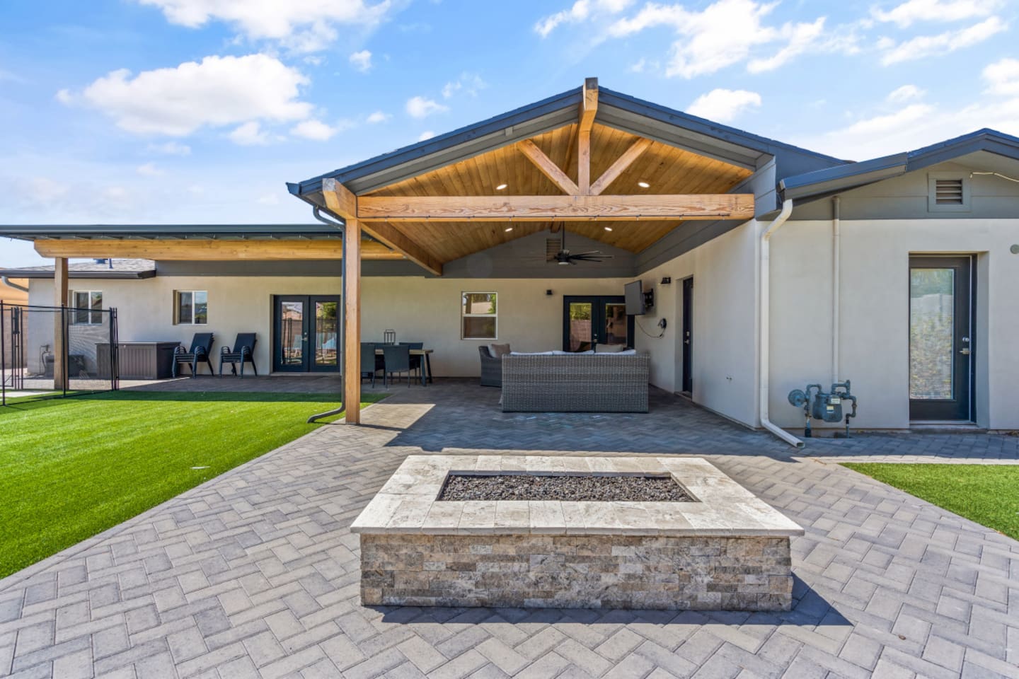 Backyard fire pit area with covered lounge seating, warm patio lighting, and sunset views.