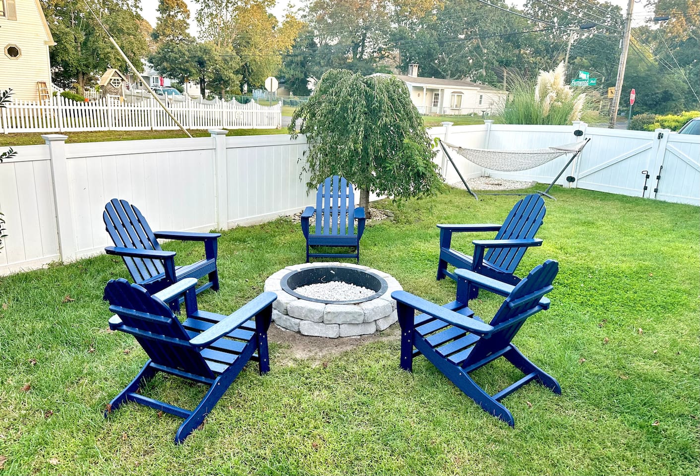 The perfect spot for s'mores and stories! This backyard setup features a cozy stone fire pit surrounded by classic blue Adirondack chairs. There’s even a hammock in the corner for those lazy afternoon naps in the sun.