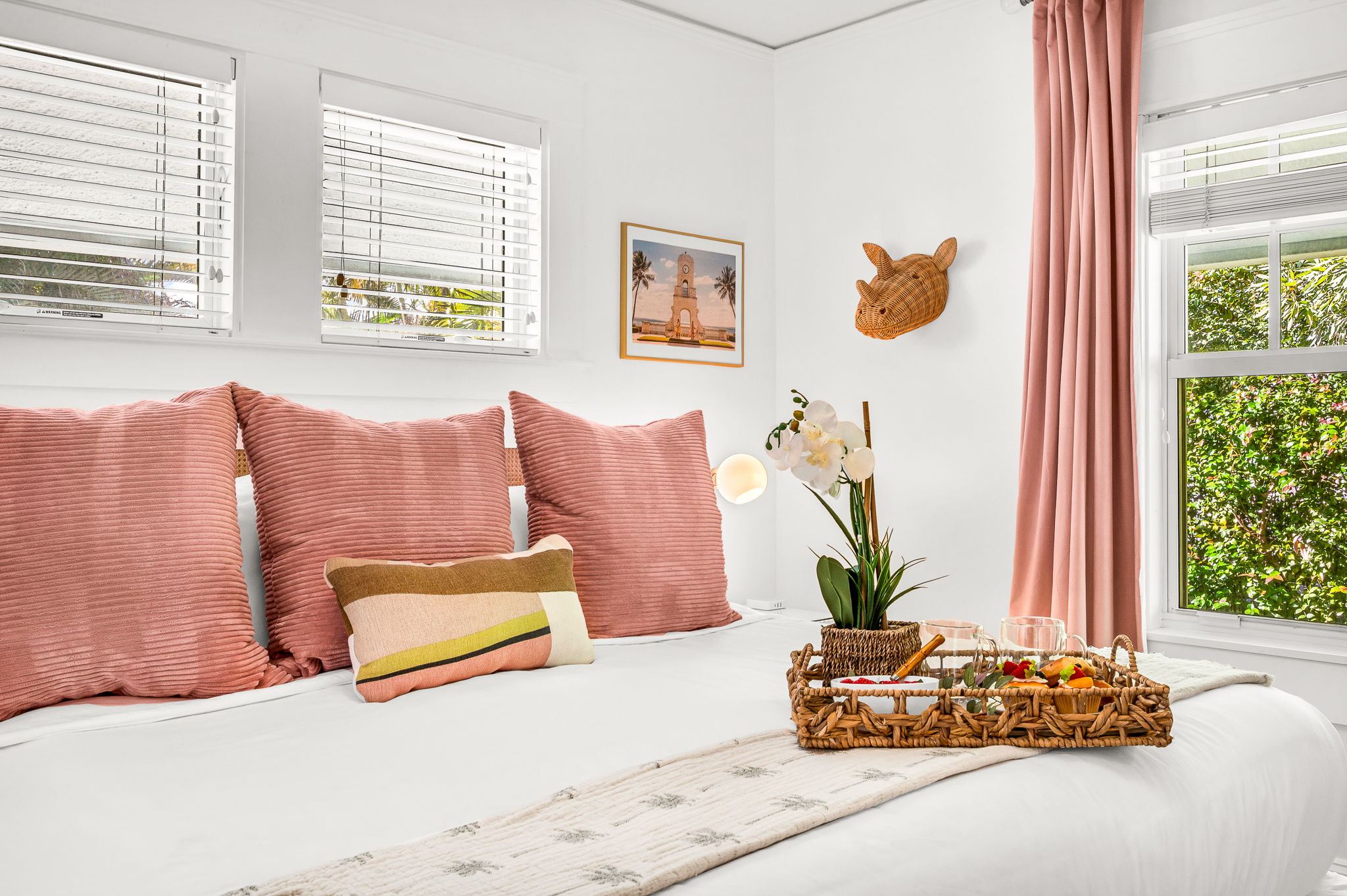 Primary bedroom with a king bed, smart TV, and ensuite bath featuring an antique soaking tub and modern shower. Cane rattan headboard, blackout drapes, and Palm Beach art add charm. Opens to the 4th bedroom, ideal for a private family suite.