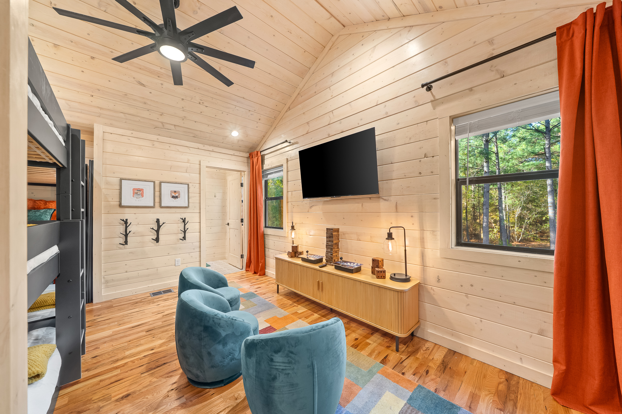 The upstairs bunkroom doubles as a media lounge with a large TV, comfy swivel chairs, and forest views.