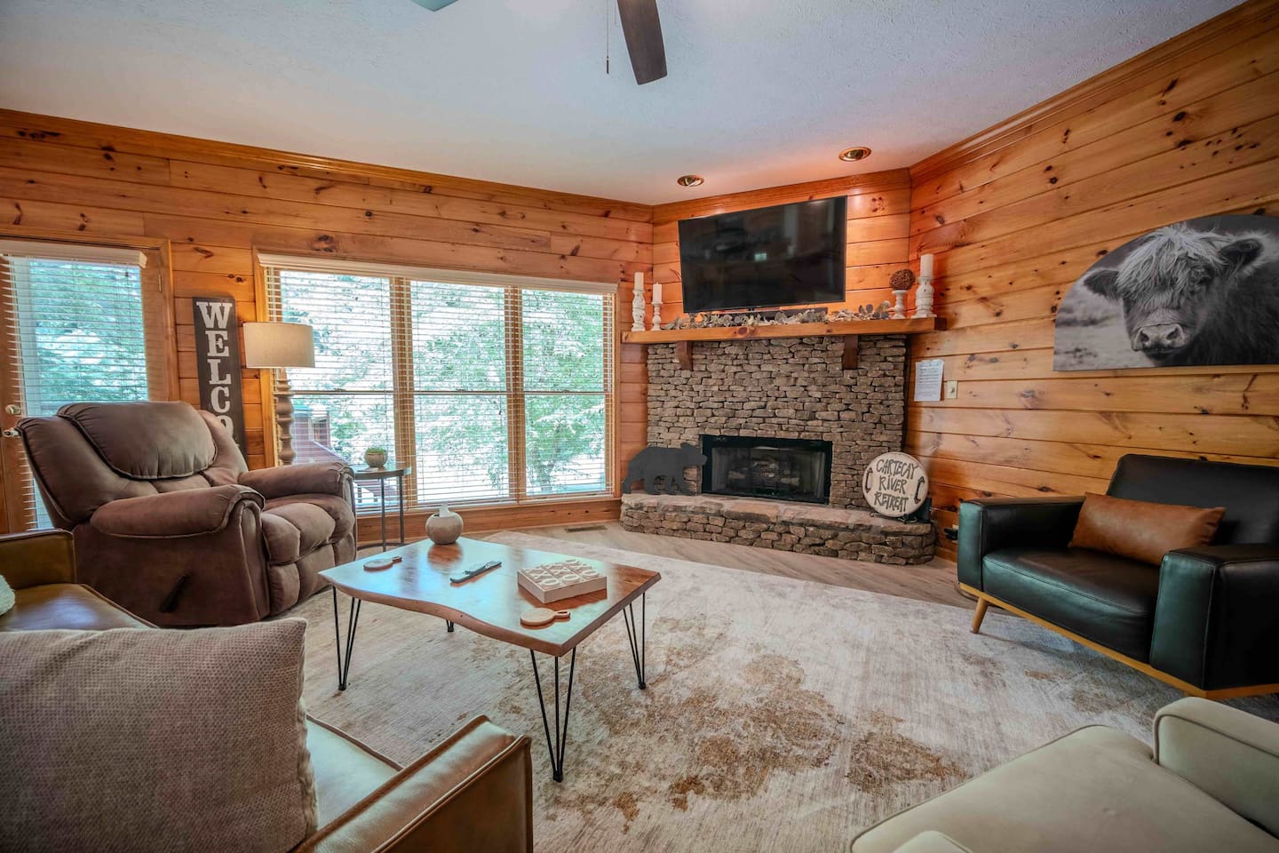 Kick back in this cozy living room featuring warm wood interiors, a stone fireplace, and serene river views through the oversized windows. 