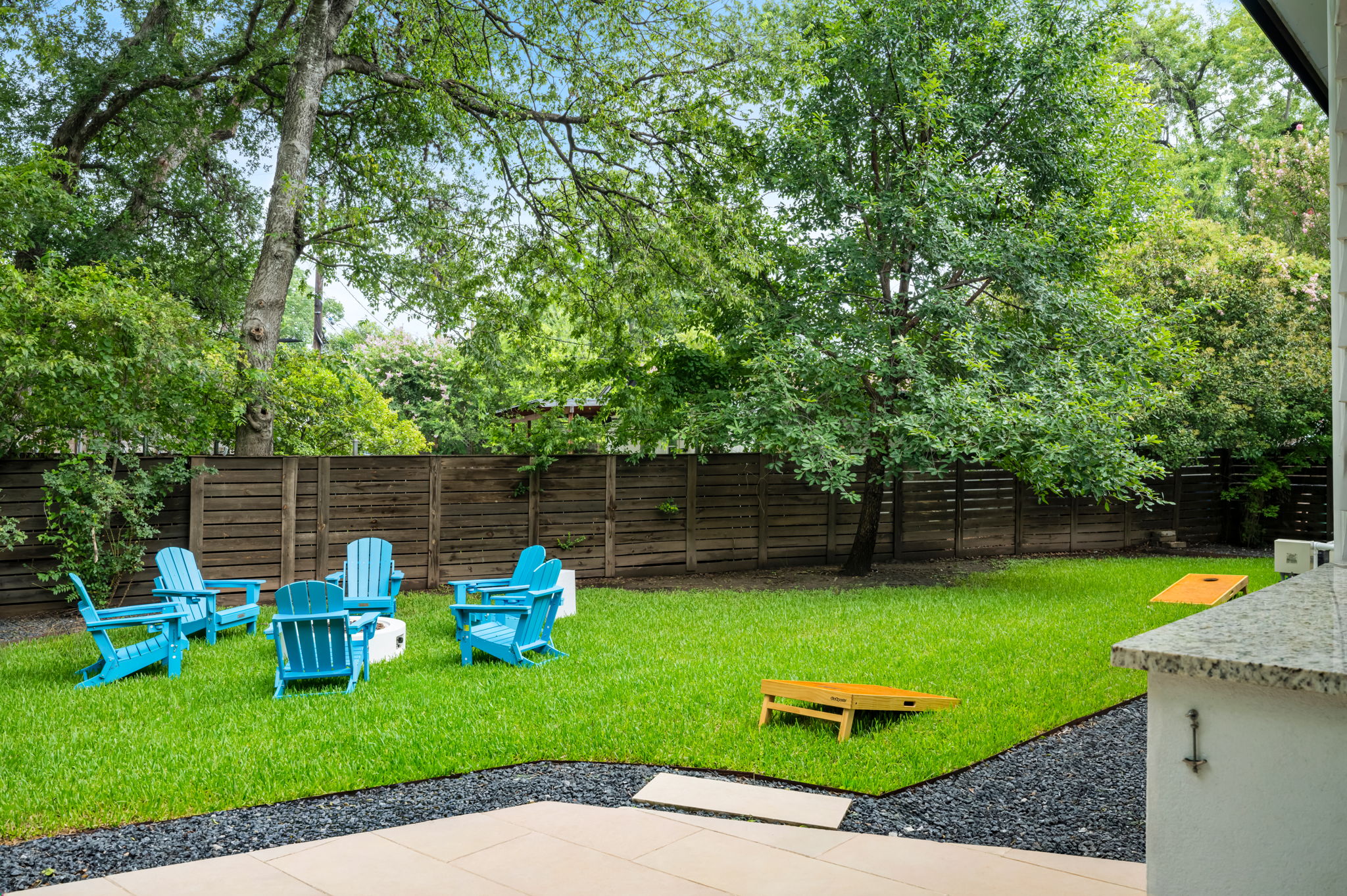 Spacious fenced backyard with plush green lawn and cozy teal Adirondack chairs — a private outdoor retreat surrounded by mature trees.