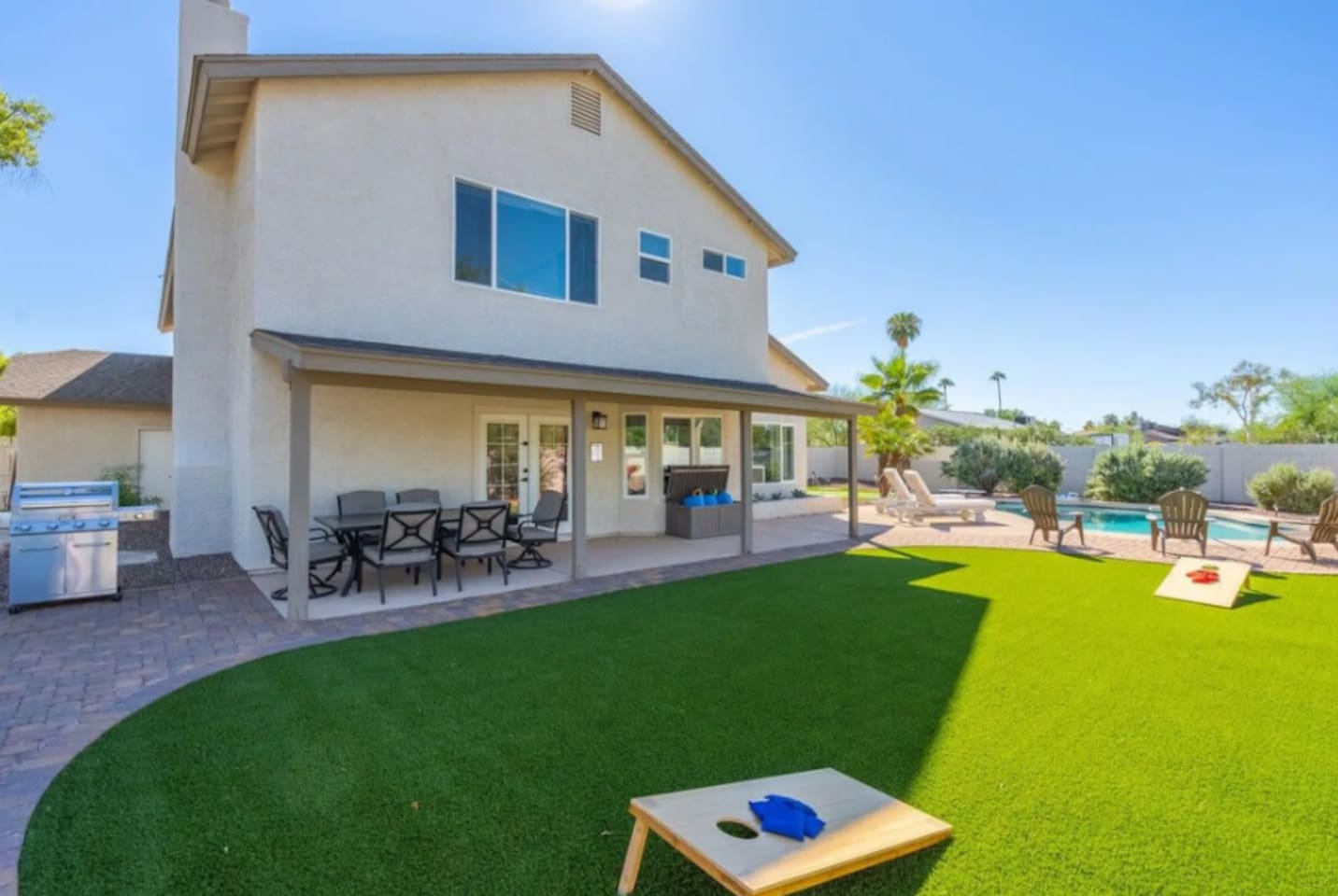 Modern home with expansive lawn, covered patio, outdoor kitchen, and sparkling pool—perfect for entertaining and games.
