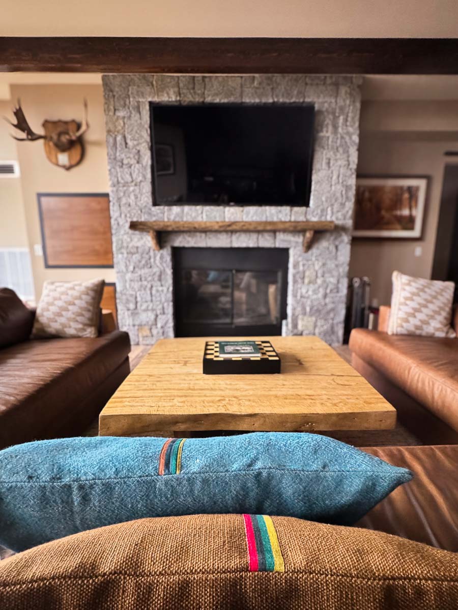 The Tavern Room at Sunset Falls &mdash; stone fireplace, antlers, and layered textile pillows on a wide leather sectional