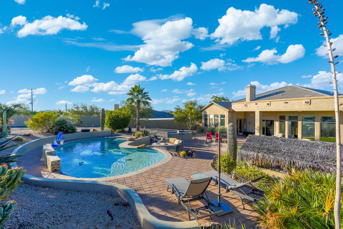 Resort-style pool with a basketball hoop, surrounded by desert landscaping and blue-sky views.