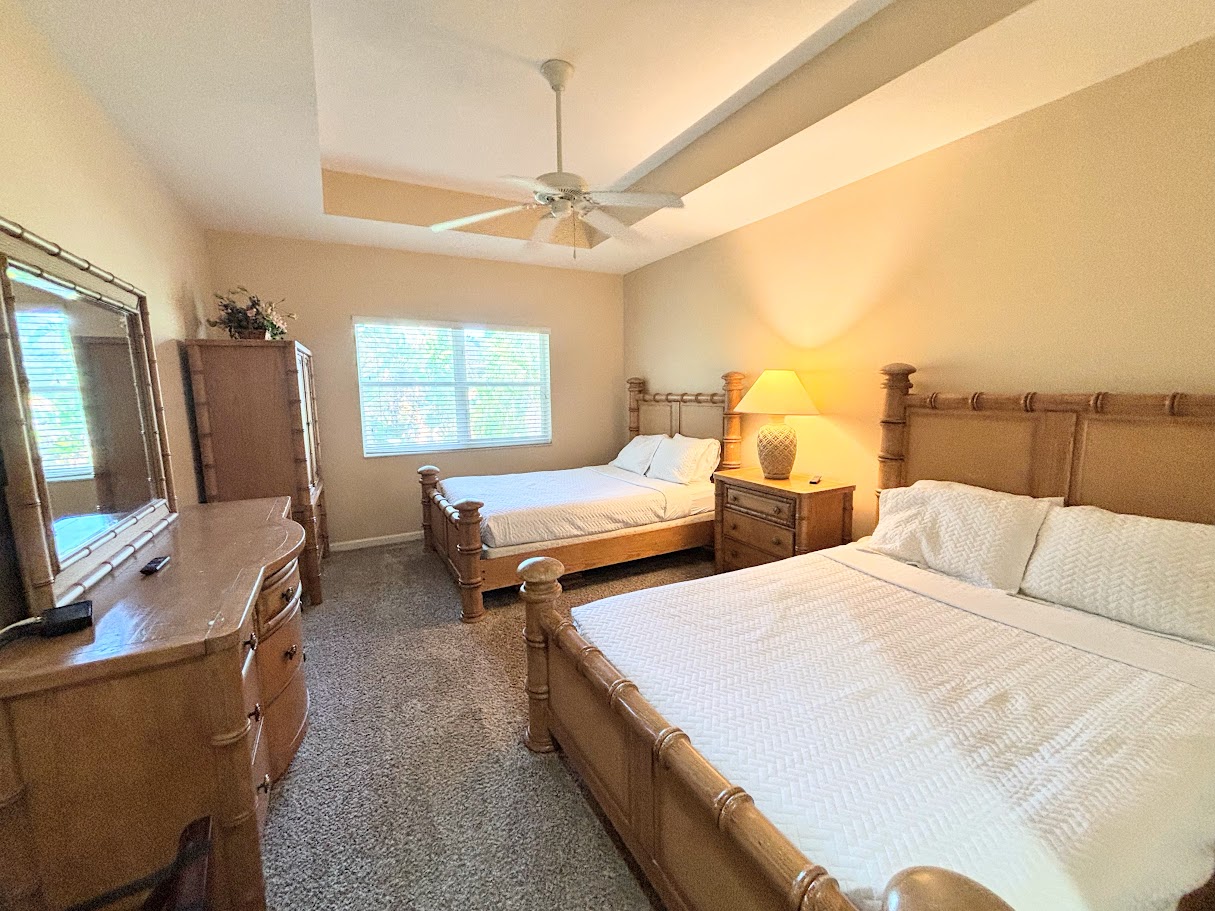 Spacious bedroom featuring two comfortable beds, tray ceiling with ceiling fan, cozy seating area, and plenty of natural light.