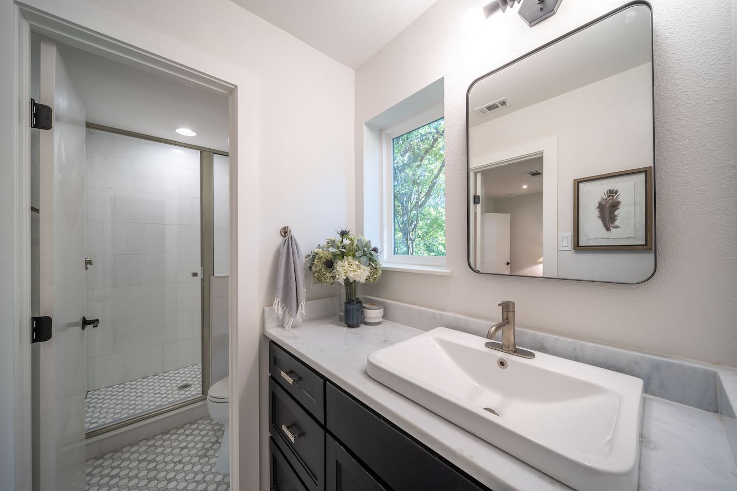 A full view of the Bedroom 2 ensuite bathroom showcases the walk-in shower, marble surfaces, and contemporary design elements. The space feels bright, fresh, and quietly luxurious. You'll have access to shampoo, conditioner, bodywash, and hand soap. 