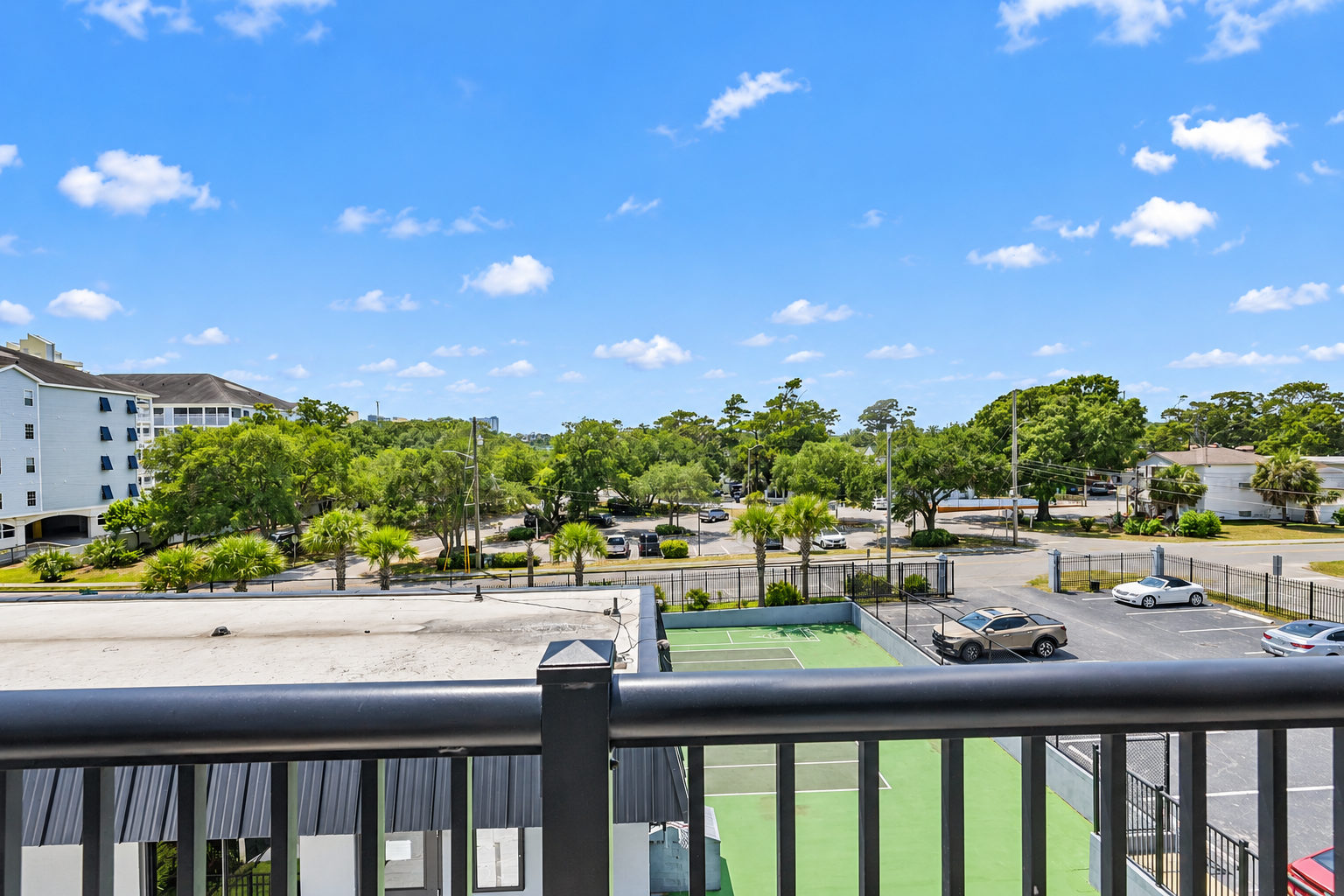 Covered balcony with table seating, chairs, and a treetop view over the Holiday Towers area.