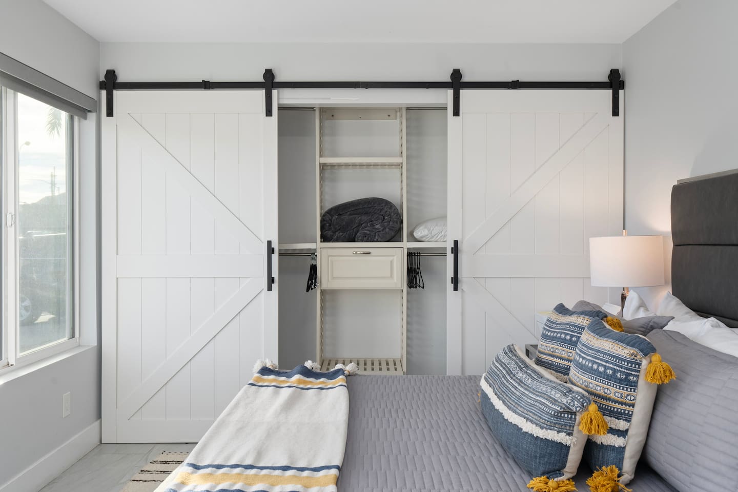 Slide open the barn doors to reveal a tidy closet with built-in shelves, extra pillows, hangers, and cozy blanket options.

