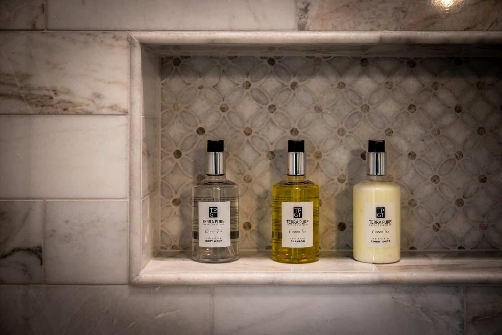 Marble shower niche with provided shower gel, shampoo, and conditioner.
