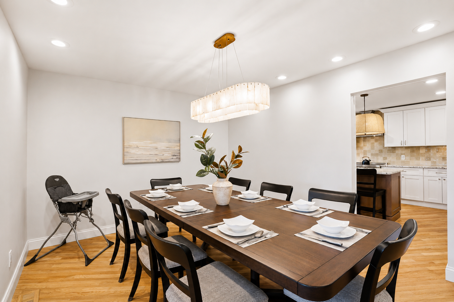 Elegant dining room with a large table, modern seating, and bright chandelier lighting. Clean, stylish space ideal for family meals and entertaining.
