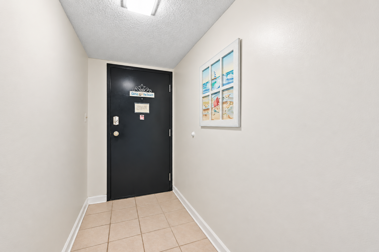 Entry hallway with tiled floor, beach-themed wall art, and direct access to the condo door.