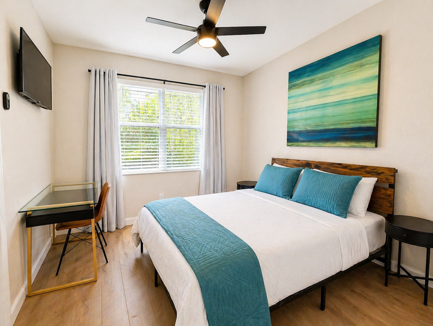 Bright and inviting bedroom with a comfortable bed, fresh linens, and modern coastal décor. Includes a dedicated workspace, wall-mounted TV, and plenty of natural light—perfect for both relaxing and getting things done.
