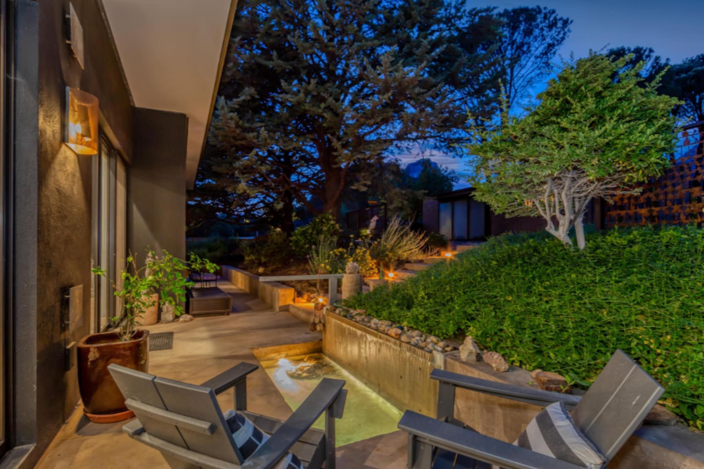 Cozy evening patio with lounge chairs overlooking a softly lit water feature and lush landscaped garden.