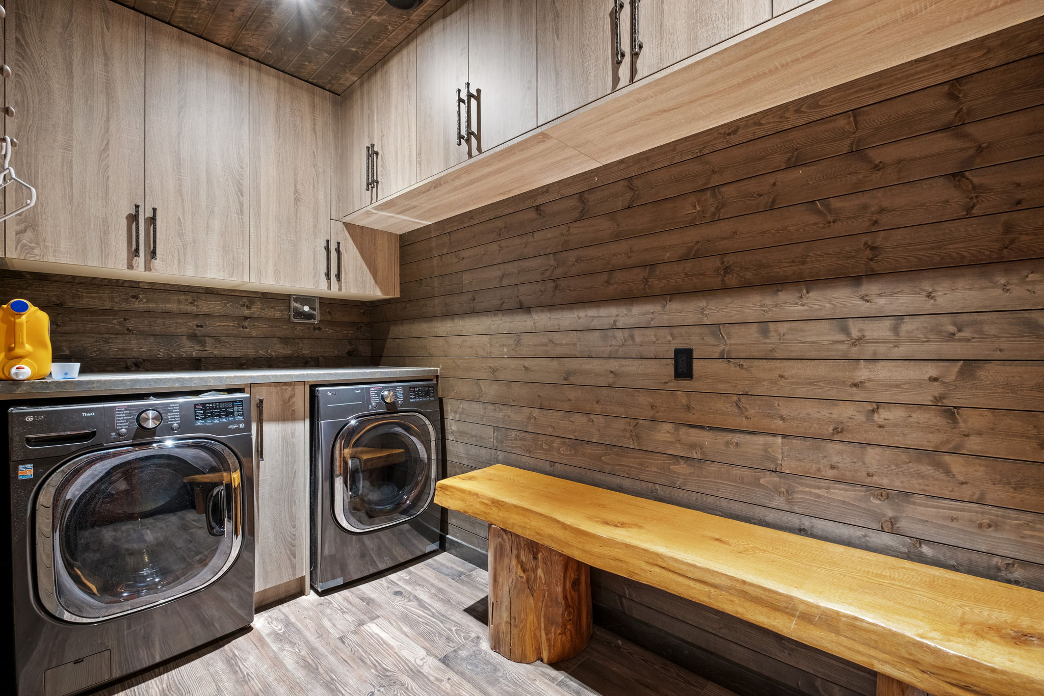 Fully equipped laundry room with premium LG washer/dryer, ample cabinetry, and a natural wood bench for gear or winter clothing.