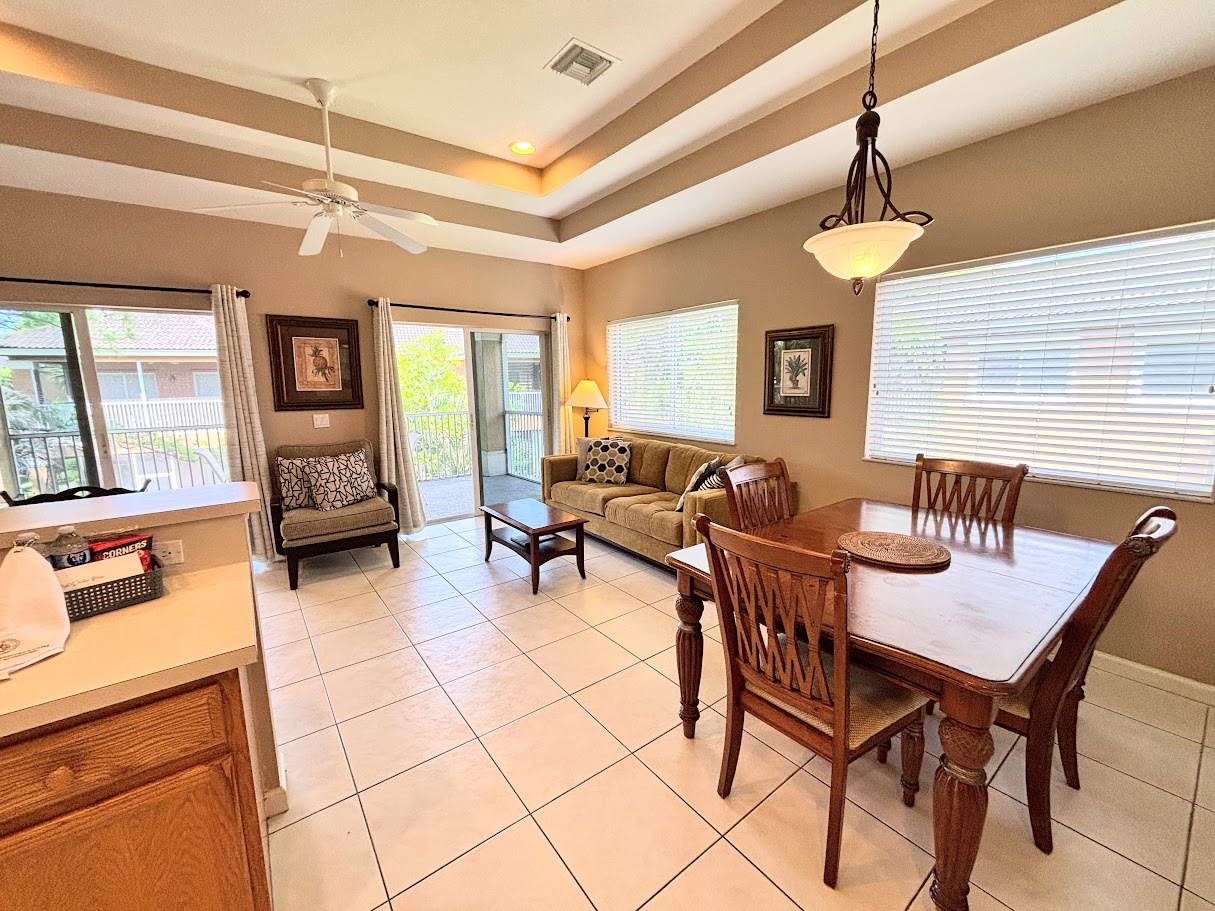 Open and inviting dining and living space with tile flooring, tray ceilings, plenty of natural light, and sliding glass doors opening to a private balcony.