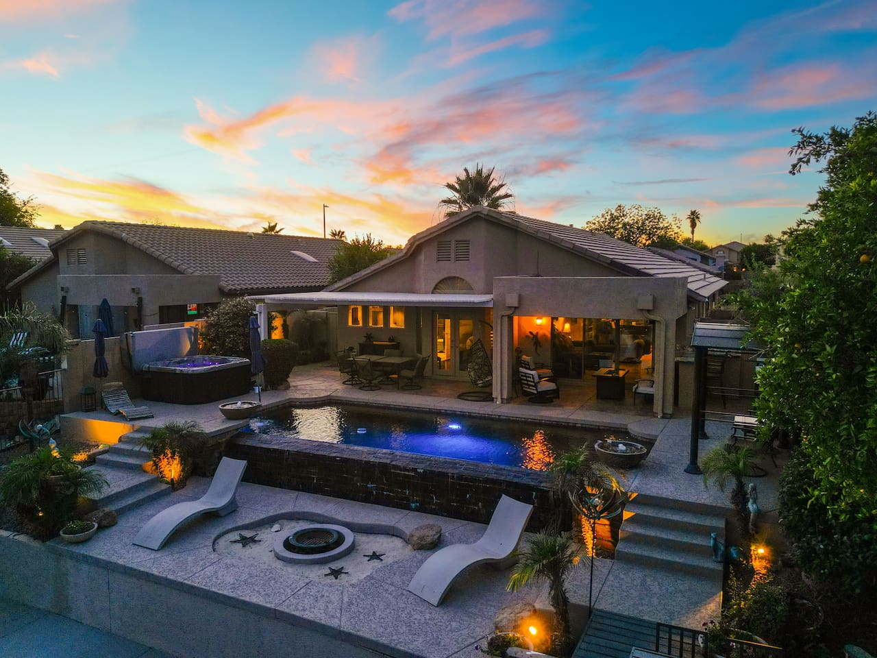 An aerial view at golden hour reveals the full picture — sparkling pool, bubbling hot tub, fire pit terrace, and a warmly lit covered patio, all coming together for the ultimate Arizona backyard experience.