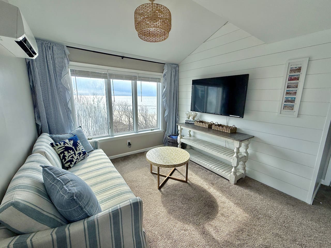Unwind in this cozy, coastal-inspired sitting area that features comfortable striped seating, a rustic console table with a wall-mounted television, and large windows offering relaxing views for the perfect vacation escape.