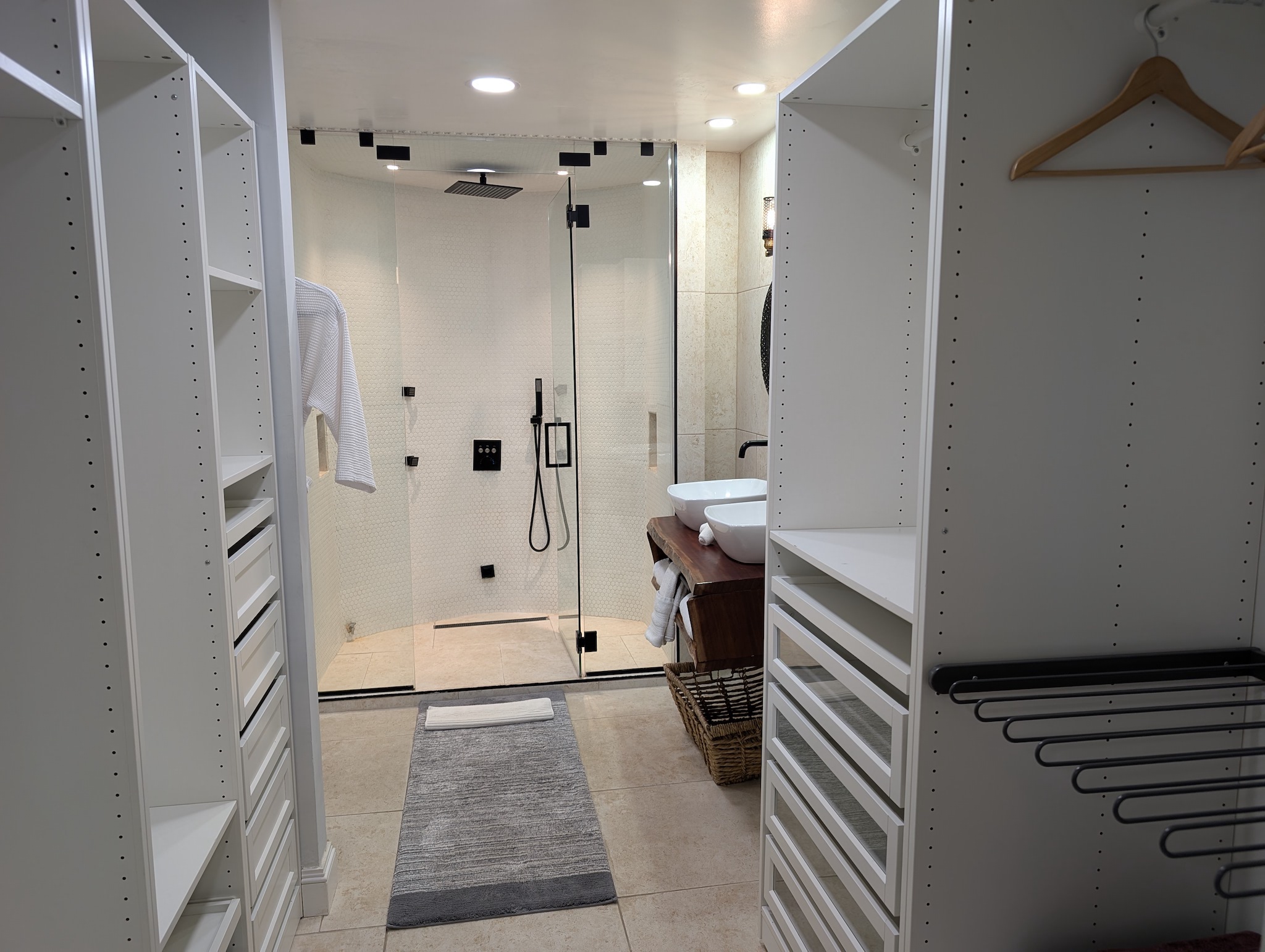 Primary bedroom ensuite bathroom at Villa Coral featuring a large walk-in closet organization system, a dual-sink vanity, and a glass-enclosed rainfall shower in Dorado, Puerto Rico.
