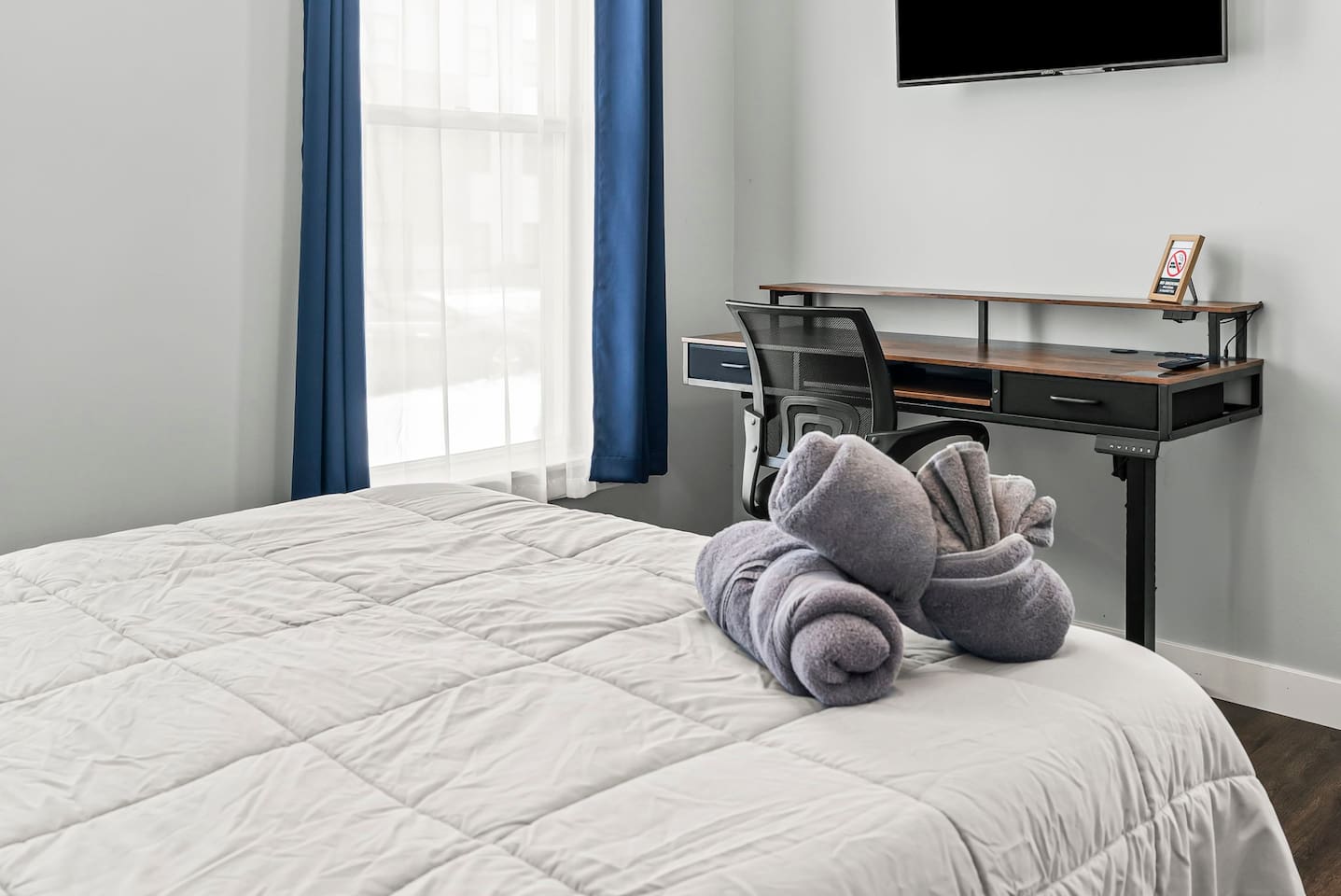 Bedroom workspace angle featuring a desk, ergonomic chair, wall-mounted TV, and natural light.