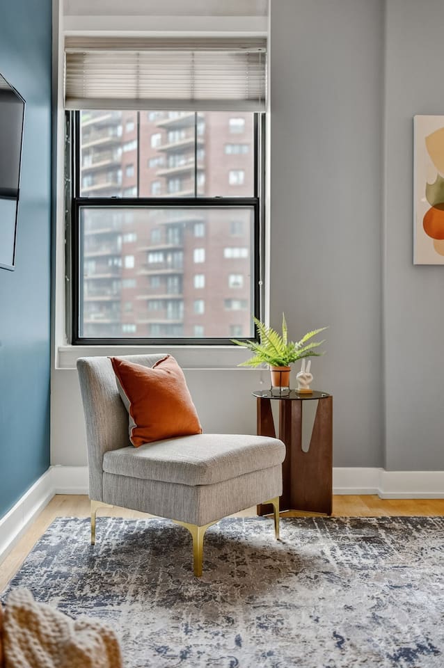 Curl up in the cozy lounge chair by the window, complete with a bright accent pillow and leafy greenery. Natural light and city views make this corner a peaceful escape for morning coffee or evening reading.