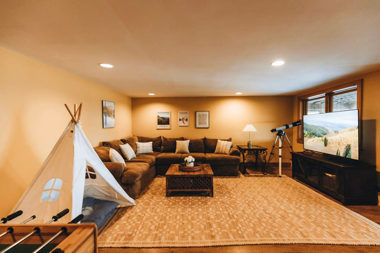 The lower level family room / game room features a large sectional sofa, football table, pingpong table, a 65" TV, a telescope for star gazing... and even a teepee for the kiddos