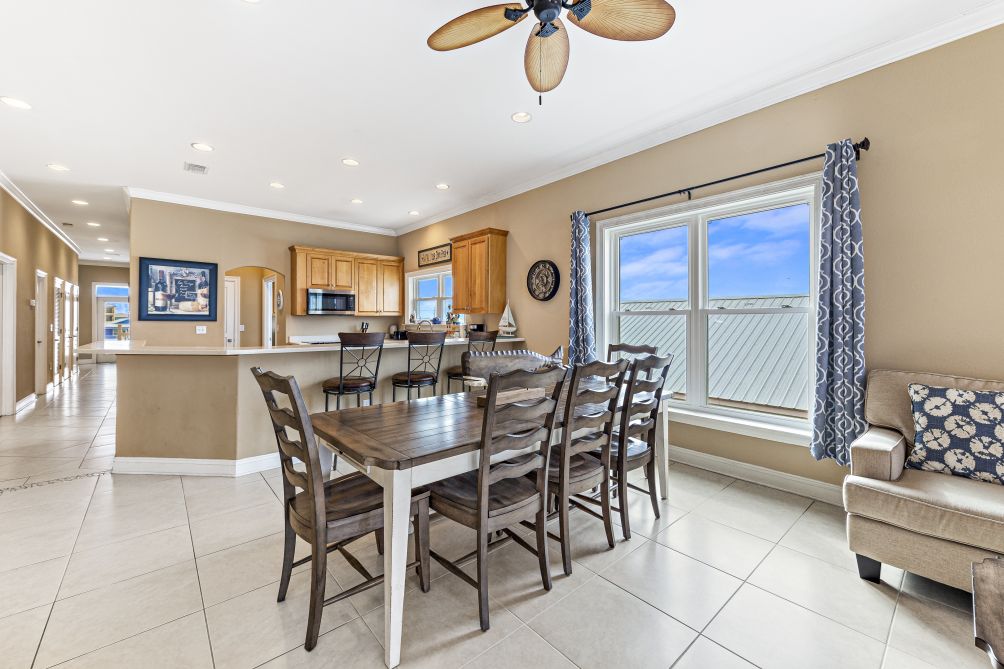 Dining table seating six beside bright windows, open to the kitchen and living area