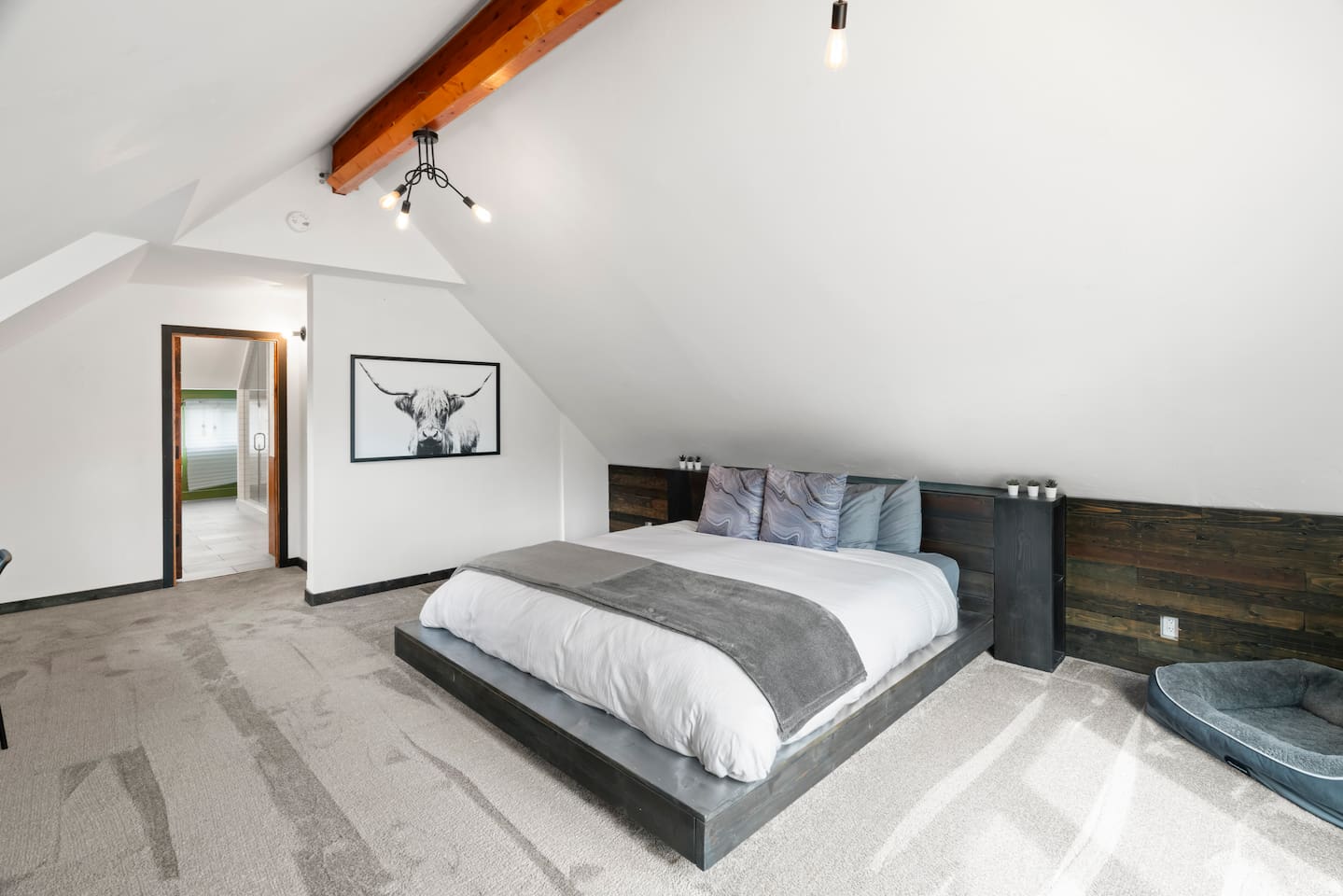 A modern yet cozy bedroom, the framed cow print adds a touch of character, while the sloped ceiling and wooden beams bring warmth. A perfect blend of comfort and style.