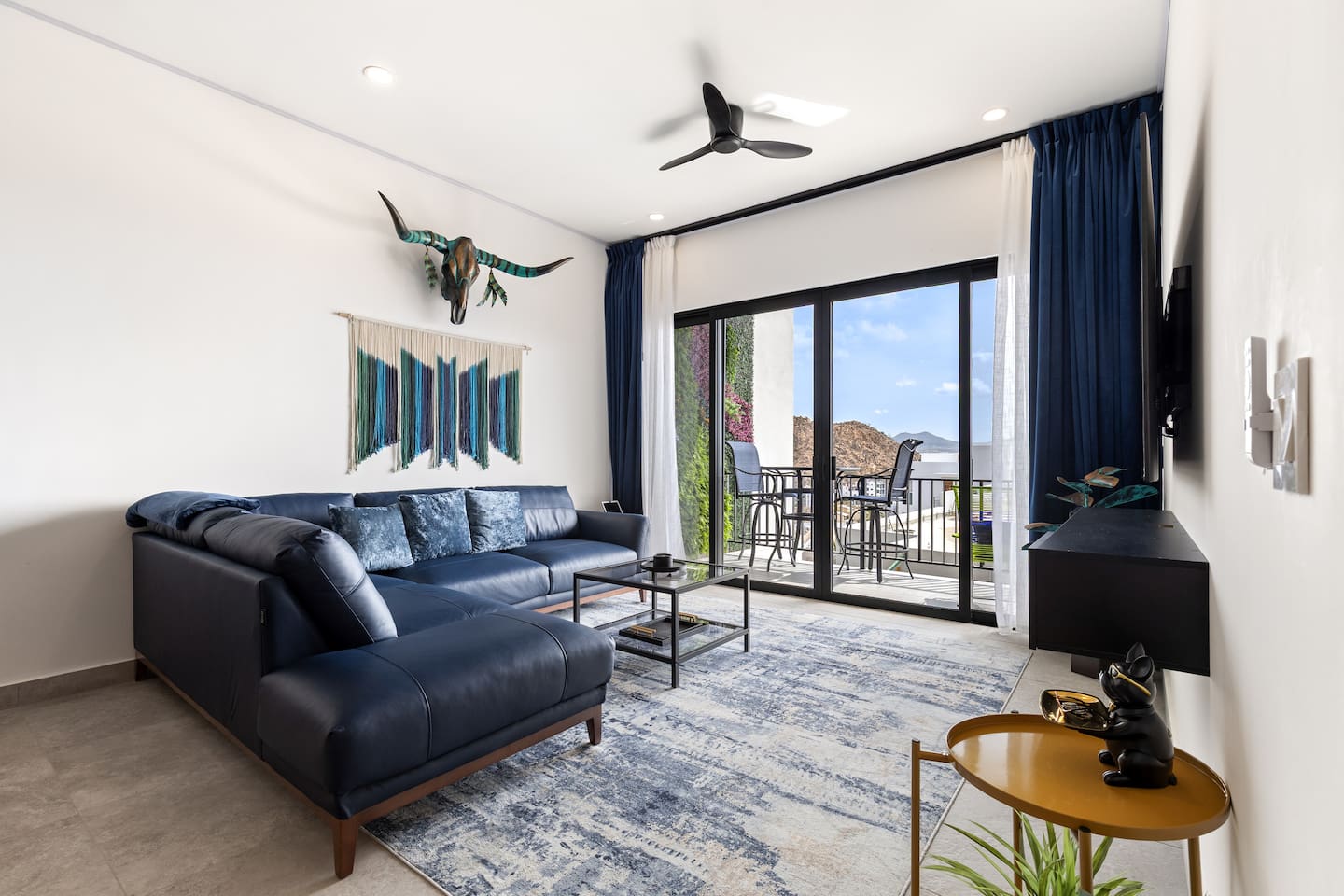 Relax in the living room facing out to the balcony, showcasing stunning local artist wall art and a luxurious left-facing blue BOAL Italian leather sectional.