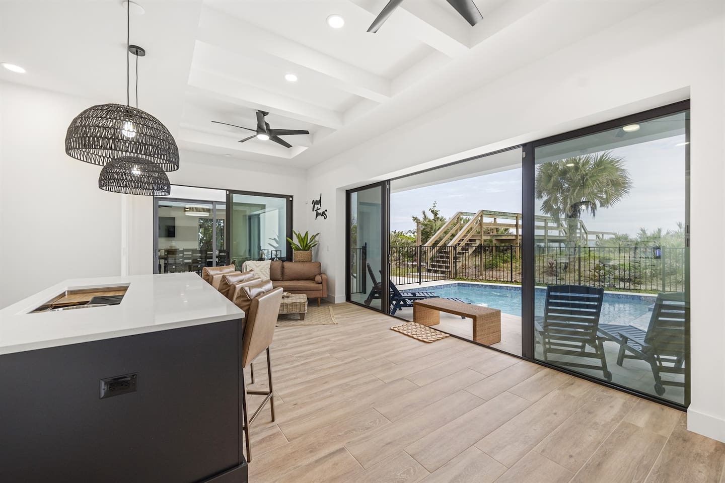 Boasts elegant chairs, granite tables with lit countertops, a chandelier fan, sleek flooring, and a beautifully decorated sofa. The large sliding door reveal a stunning outdoor view, blending indoor luxury with natural beauty.