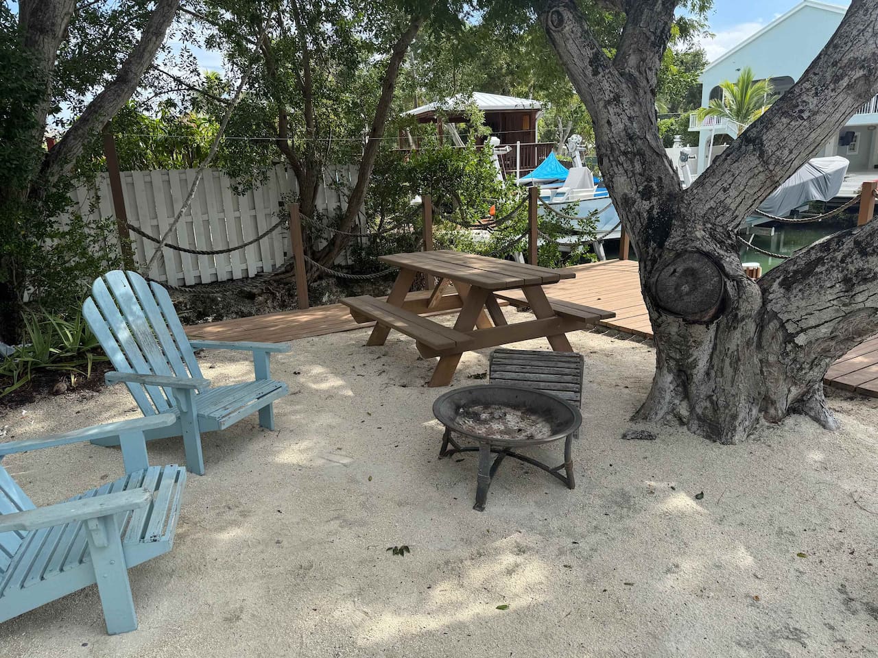 Sandy and shady area with chairs, picnic table and fire pit