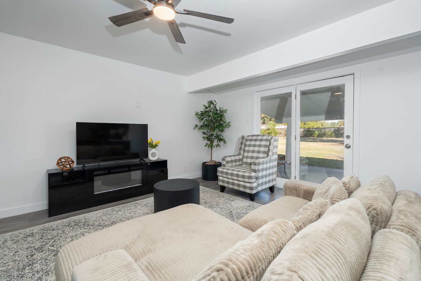 Spacious living room with hardwood floors, comfortable plush couch, a Smart TV with streaming services, and a ceiling fan. Enjoy fast Wi-Fi, natural light, and an open layout ideal for relaxing or remote work.
